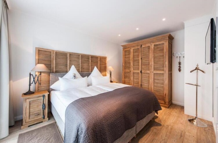 Seitlicher Blick auf ein helles Hotelbett, das Zimmer ist mit viel Holz ausgestattet.