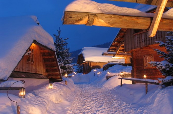 Laternen beleuchteter Weg voller Schnee zwischen Holzchalets  bei Abenddämmerung