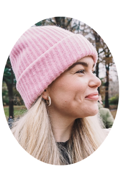 Anna Brouwers von "The Travelogue" posiert freudig lächelnd mit einer rosa Beanie-Mütze