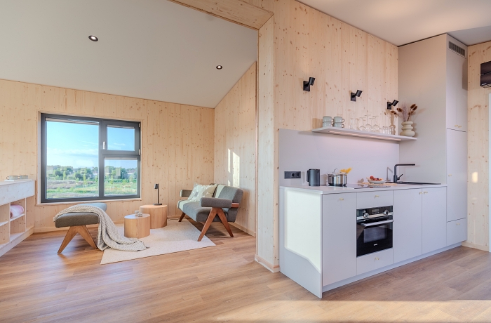 Modernes Baumhaus-Apartment mit offenem Wohnkonzept, heller Küchenzeile und nachhaltiger Holzarchitektur. Große Fensterflächen, natürliche Materialien und die stilvolle Einrichtung schaffen eine warme, naturnahe Atmosphäre und verbinden modernen Komfort mit einem entspannten Aufenthalt inmitten der Landschaft.