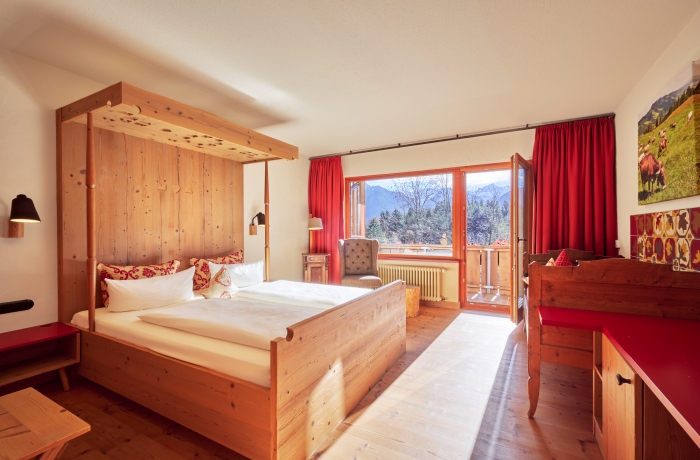 Gemütliches Hotelzimmer mit Holzbett, roten Akzenten, Balkon und Blick auf die Allgäuer Berge.