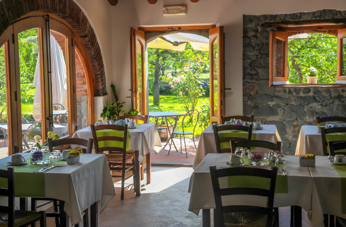 Mediterranes Hotelrestaurant mit rustikalem Ambiente und Blick in den grünen Garten.