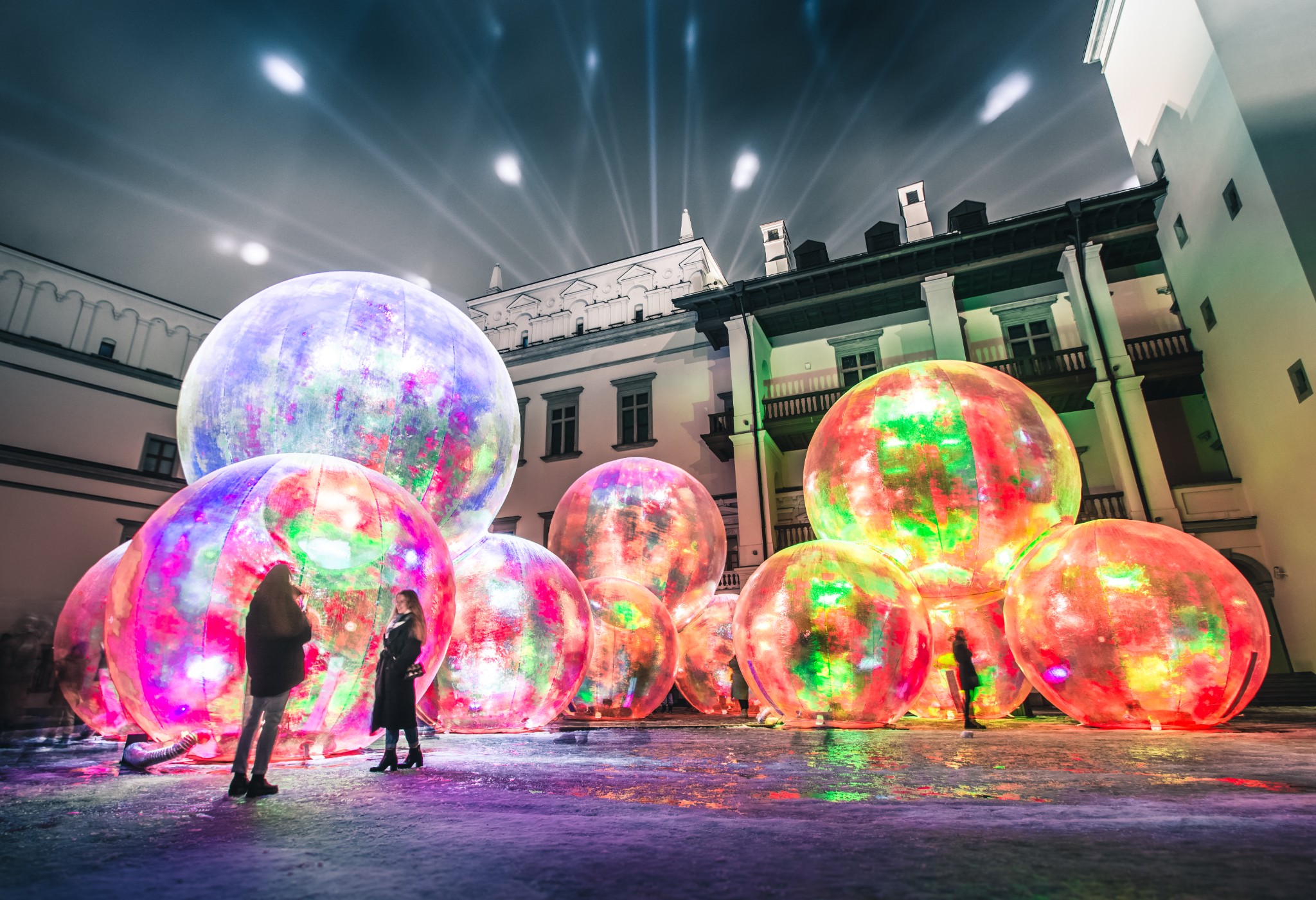 Unter dem Nachthimmel in einem Innenhof stehen als Installation bunt in Neonfarben beleuchtete, durchsichtige Kunststoffbälle, davor posieren Personen für Bilder.