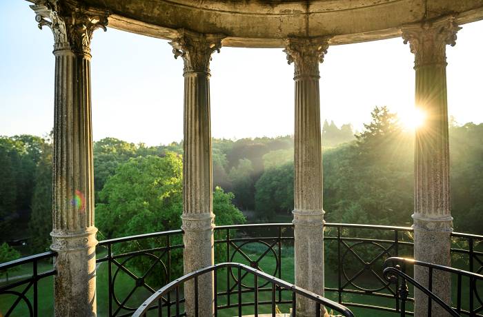 Sunset Spots: Blick vom Schlossturm durch schmucke Säulen auf den grünen Wald, über dem die Sonne untergeht