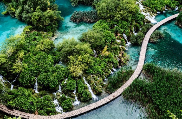 Auf dem Bild sieht man blaues Wasser und grüne Büsche, welche durchzogen wird von einem langen Steg.
