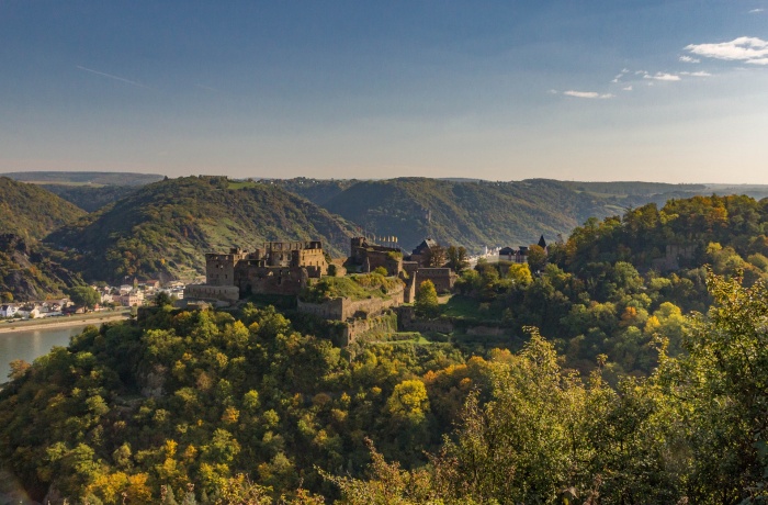 Man sieht eine altertümliche Burg auf einem Hügel, dahinter sieht man den Rhein.