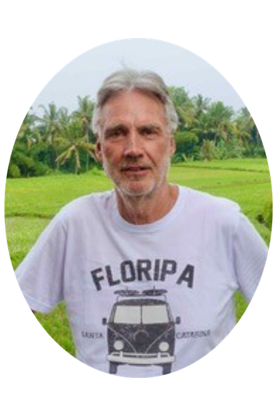 Peter Pohle posiert vor einer tropisch grünen Landschaft, im Hintergrund sind Palmen zu sehen