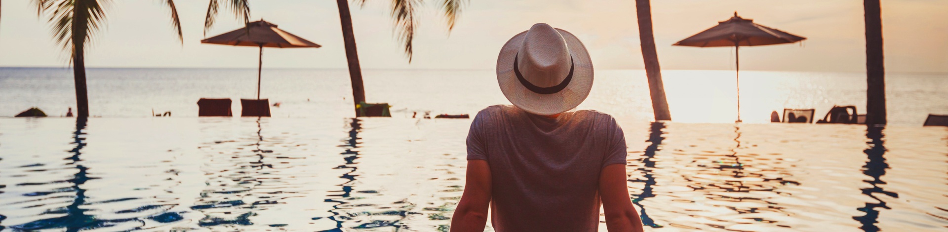 Die Top 50 männlichen Reiseblogger: Mann mit Hut schaut auf Pool und Palmen