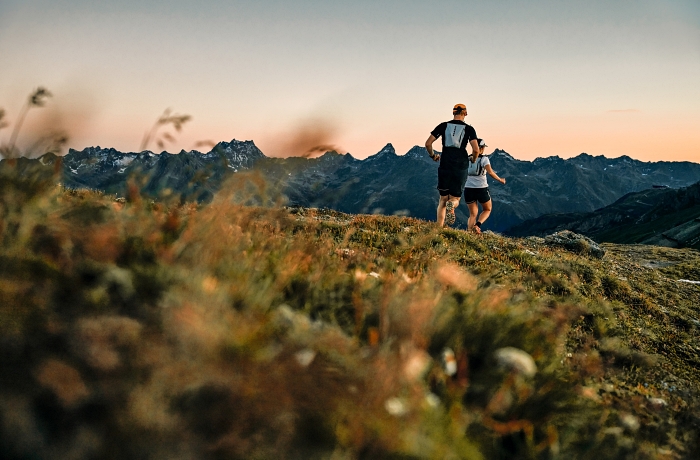 Zwei Personen beim Lauftraining in einer Abend- oder Morgenlandschaft mit Bergblick