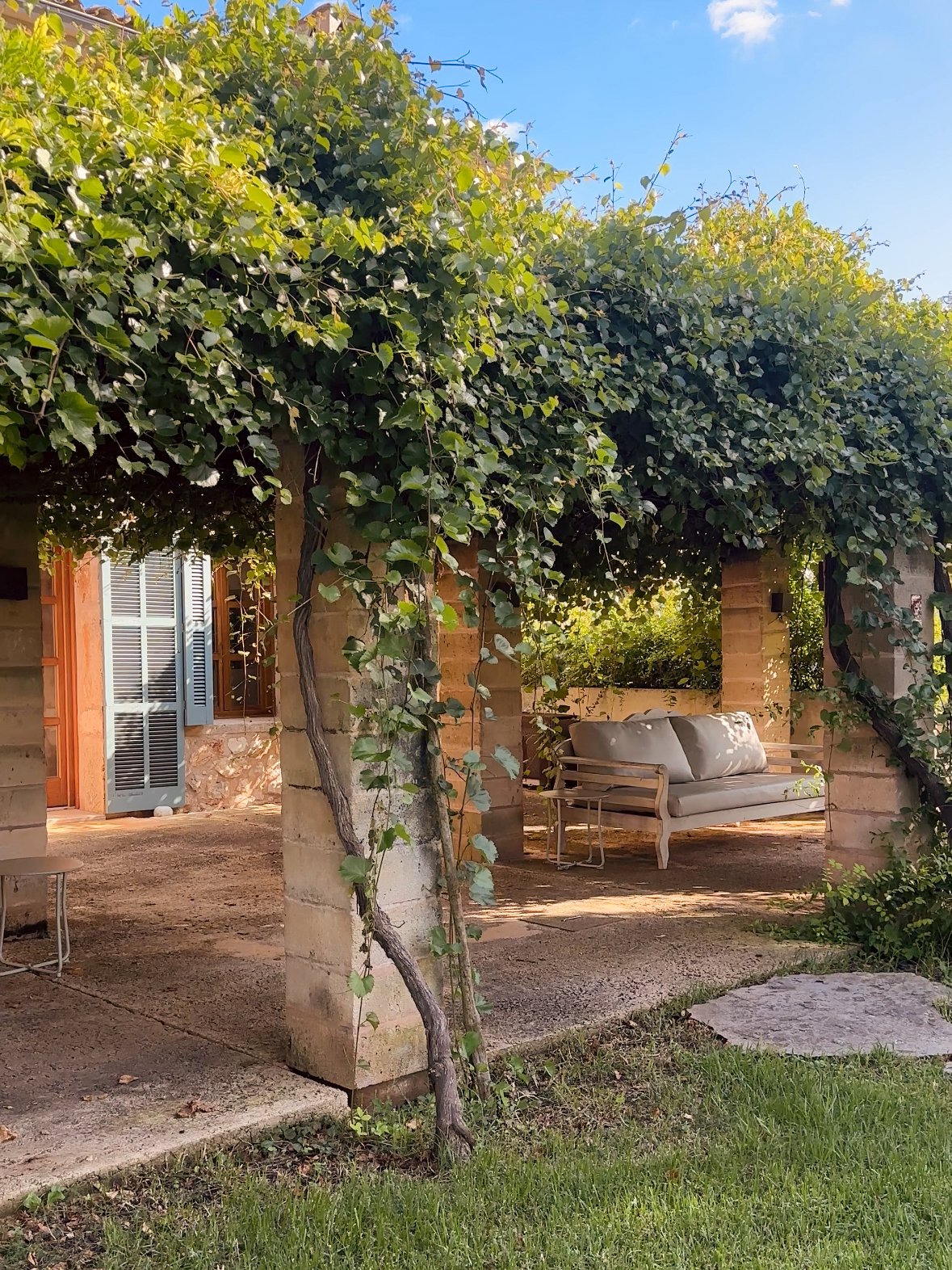 Mallorca im Sommer: Die Hitze lässt sich gut wie hier aushalten, unter dem Blätterdach und Steinsäulen, auf einer gemütlichen Gartenbank