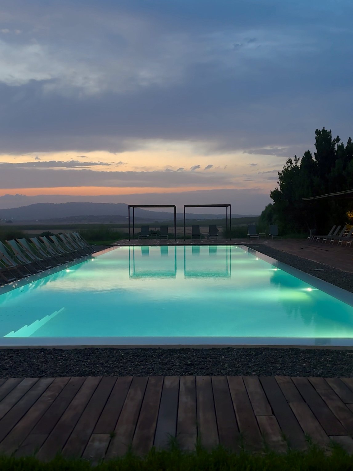 Hinter dem Pool, von Liegen gesäumt, geht atmosphärisch die Sonne unter.