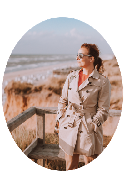 Top Reisebloggerin Sabine Bassier steht im beigen Trenchcoat am Strand von Sylt