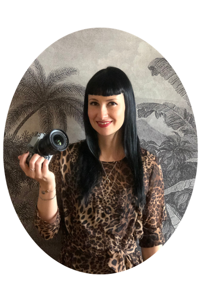 Top 50 Reisebloggerin Susi Maier posiert vor einer kunstvollen Tapete mit Palmenprint und Kamera in der Hand