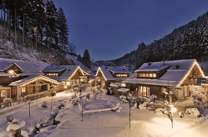 Dorf aus schneebedeckten Chalets, umgeben von Wäldern bei Nacht 