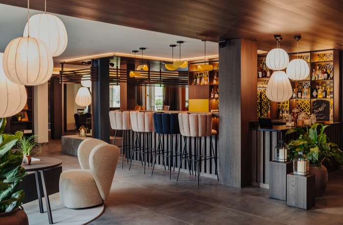 Bar mit modernen Barstühlen im Muscheldesign, im Vordergrund steht ein Ruhesessel vor einem Tisch