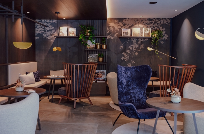 Gemütlicher Loungebereich mit diversen Stühlen & Sesseln aus Samt und Holz, tiefen Hängelampen und floraler Tapete