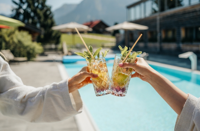 Zwei Gäste stoßen mit erfrischenden Getränken am Außenpool eines Hotels an.
